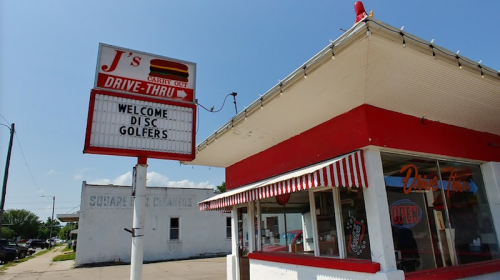 A drive-thru restaurant with a sign welcoming disc golfers, featuring a red and white striped awning.