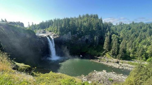 A scenic view of a waterfall cascading into a green pool, surrounded by lush trees and a clear blue sky.