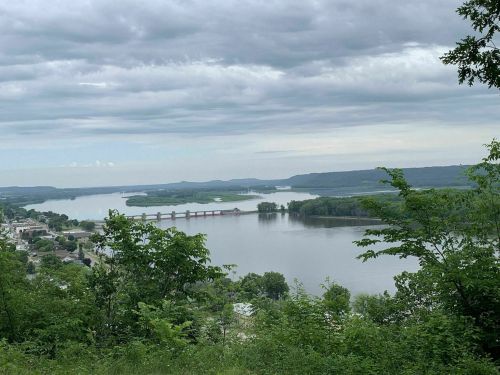 A scenic view of a river surrounded by greenery and hills under a cloudy sky.