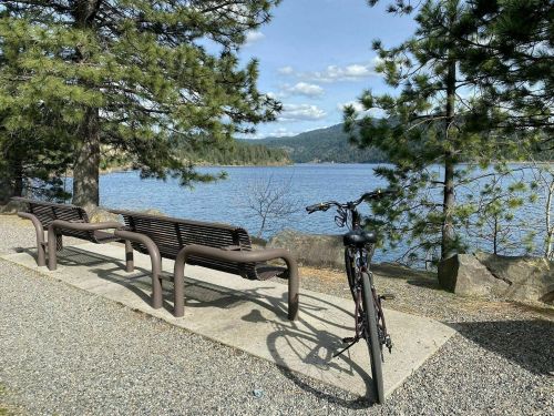 A bike parked beside two benches overlooking a serene lake surrounded by trees and mountains.