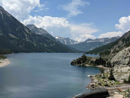 A serene lake surrounded by mountains under a partly cloudy sky, with lush greenery along the shore.