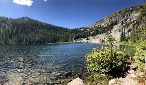 A serene mountain lake surrounded by lush trees and rocky hills under a clear blue sky.