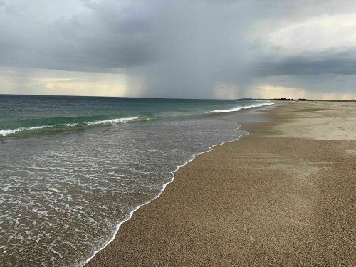 A serene beach scene with gentle waves, sandy shore, and dark clouds in the distance hinting at rain.