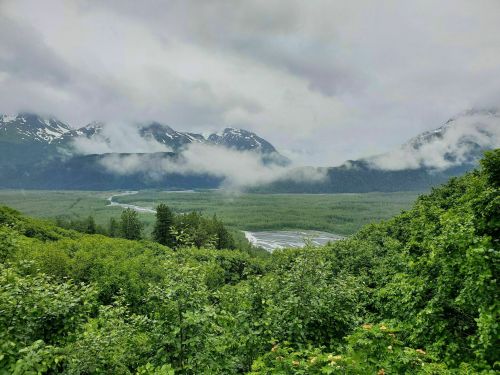 A lush green valley surrounded by mountains, with clouds and mist hovering over the landscape.