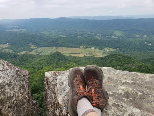 A pair of hiking shoes resting on a rocky ledge, overlooking a lush green valley and distant mountains.
