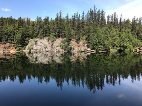 A serene lake reflecting a forested shoreline under a clear blue sky.