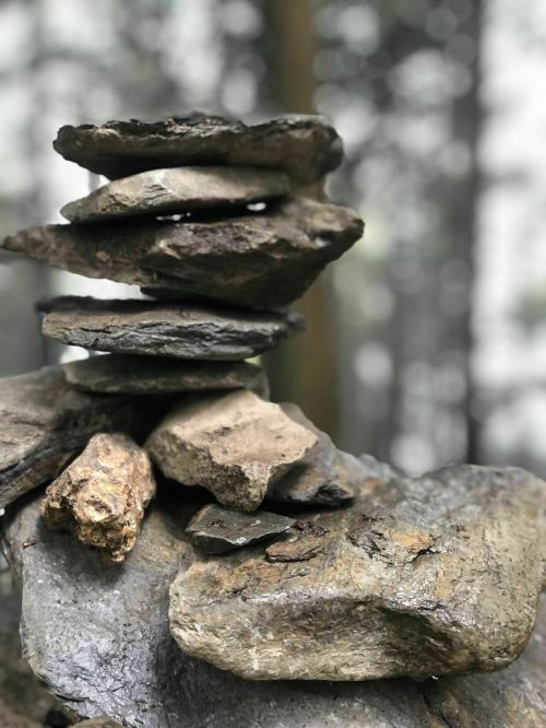 A stack of various stones balanced on top of each other, set against a blurred forest background.