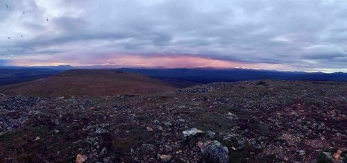 A panoramic view of a rugged landscape under a cloudy sky, with distant mountains and a hint of sunset colors.