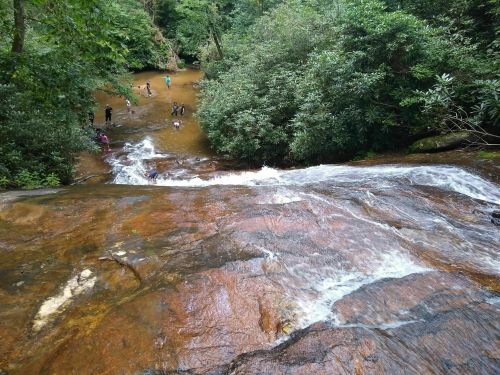 A waterfall cascades over rocky terrain, with people enjoying the water in a lush, green forested area.