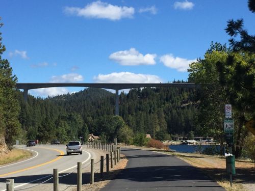 A scenic view of a road leading to a bridge over a forested area, with a lake visible on the right.
