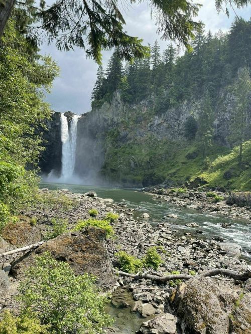 A scenic view of a waterfall cascading down rocky cliffs, surrounded by lush greenery and a calm river.