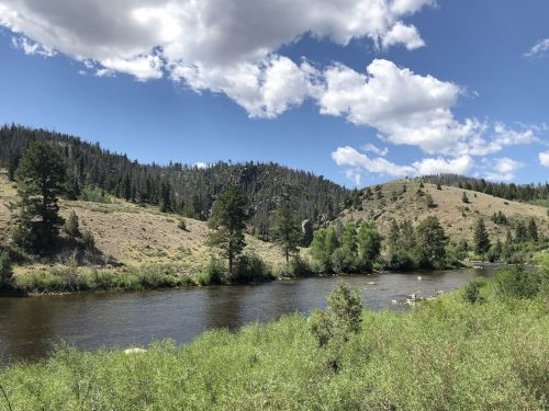 A serene river flows through a lush green landscape, surrounded by hills and trees under a partly cloudy sky.