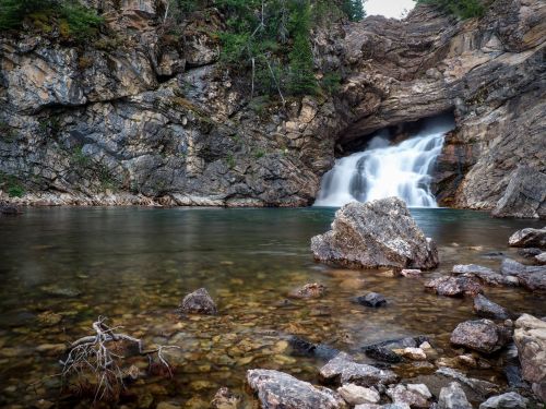 A serene waterfall cascades into a clear pool, surrounded by rocky cliffs and lush greenery.