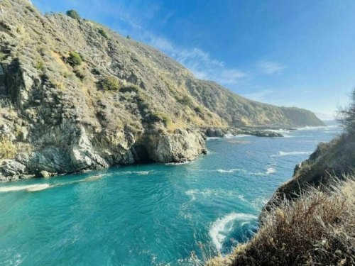 A scenic view of a turquoise ocean surrounded by rocky cliffs and hills under a clear blue sky.