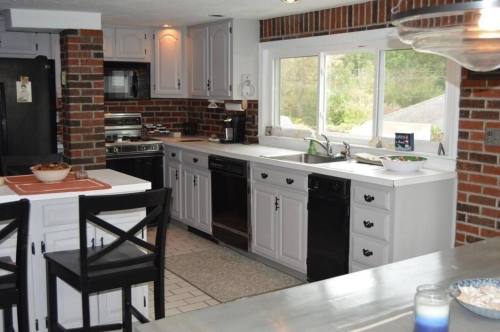 A modern kitchen featuring brick walls, white cabinets, and stainless steel appliances, with a large window for natural light.