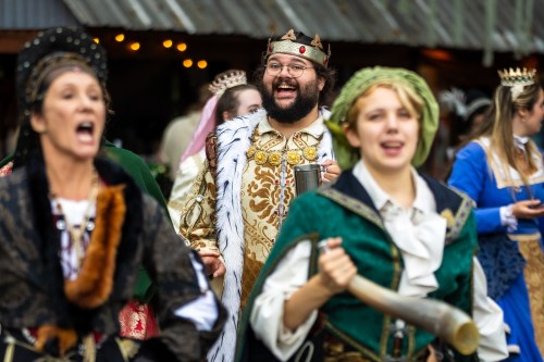 A joyful group in medieval costumes, with a man in a crown and fur cape, celebrating at a festive event.