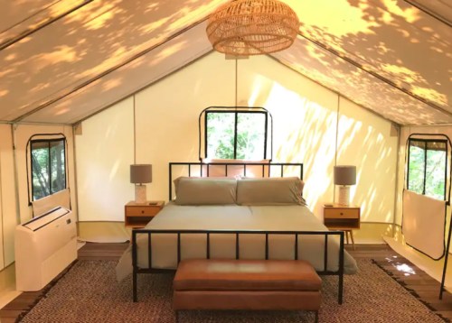 Cozy glamping tent interior with a bed, nightstands, lamps, and natural light filtering through the windows.