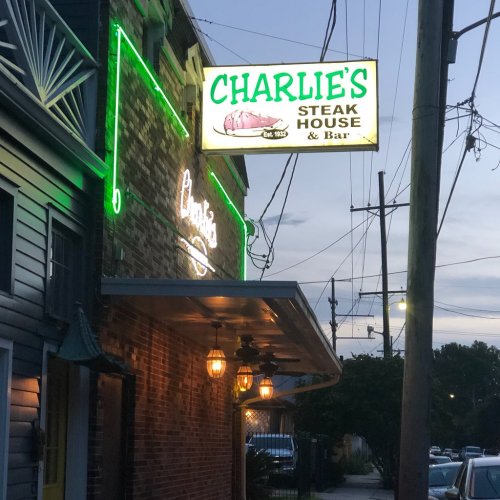 Sign for Charlie's Steak House & Bar, illuminated in green, with a brick building and evening sky in the background.