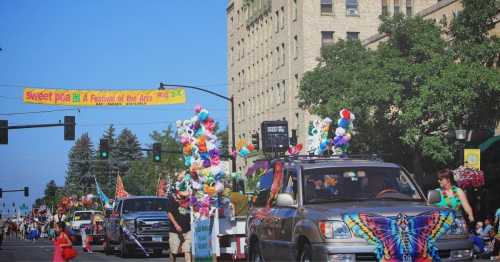 A festive parade with colorful floats and decorations, set against a sunny street and a banner for the Sweet Pea Festival.