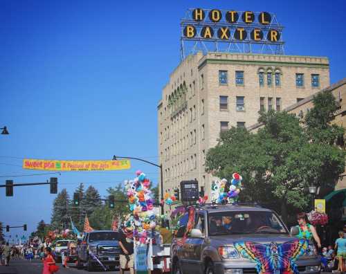 A vibrant parade with colorful floats and decorations in front of Hotel Baxter under a clear blue sky.