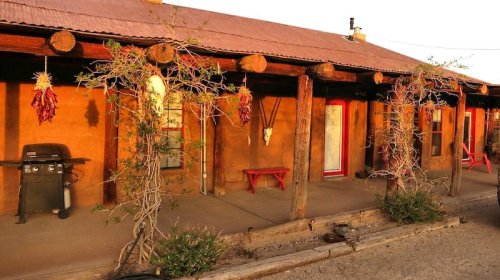 Adobe-style building with a rustic porch, hanging chili peppers, and a grill, bathed in warm sunset light.
