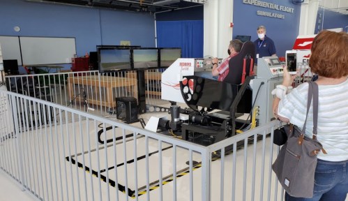 A person uses a flight simulator in a fenced area, with screens displaying landscapes in the background.