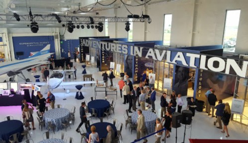 A spacious event venue with guests mingling around tables, featuring an airplane and a large "Adventures in Aviation" sign.