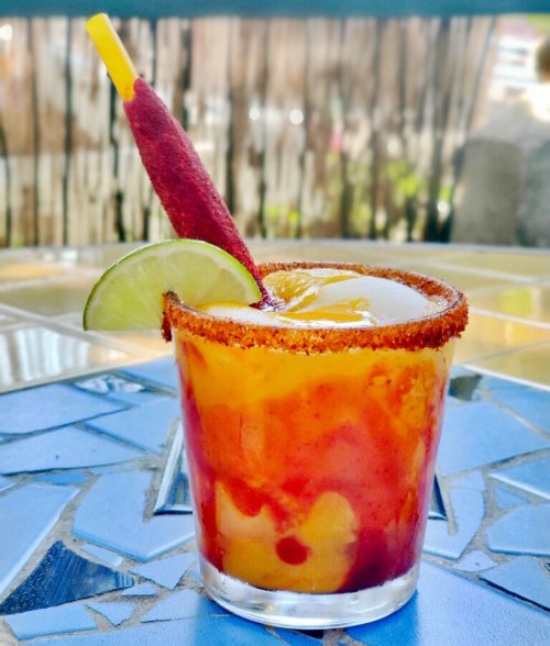 A colorful cocktail in a glass with a salted rim, garnished with a lime slice and a colorful straw.