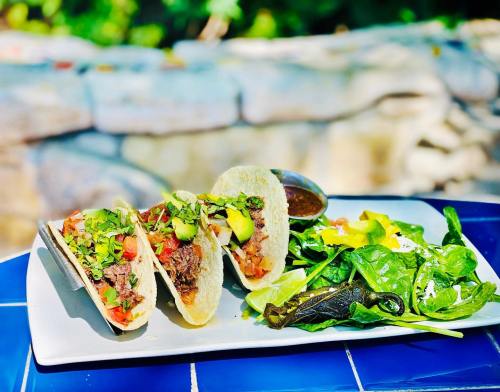 Three tacos filled with beef, tomatoes, and avocado, served with a side of fresh spinach salad and dressing.