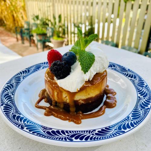 A slice of cheesecake topped with whipped cream, berries, and caramel sauce, served on a decorative plate.