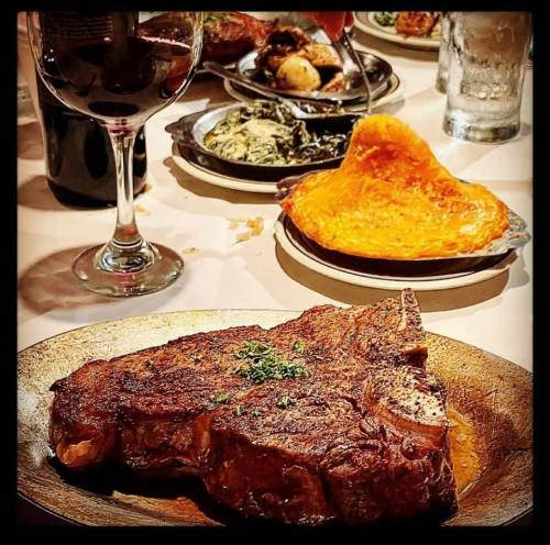A juicy steak on a wooden plate, accompanied by sides and a glass of red wine in a cozy dining setting.
