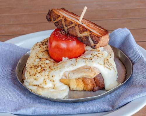 A savory dish featuring bread topped with creamy sauce, a slice of tomato, and crispy bacon on a metal plate.
