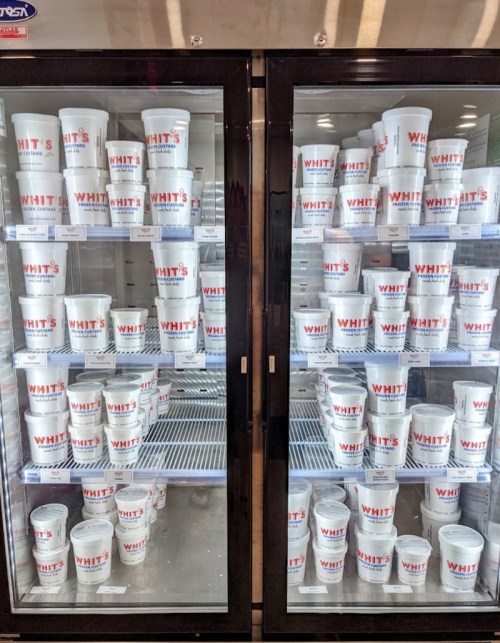 Two glass-front refrigerators filled with white containers labeled "WHIT'S" stacked neatly inside.