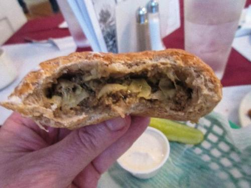 A hand holding a flaky pastry filled with ground meat and cabbage, with a side of dipping sauce.