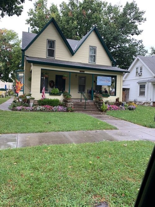 A charming yellow house with a gabled roof, surrounded by colorful flowers and greenery, featuring a welcoming porch.