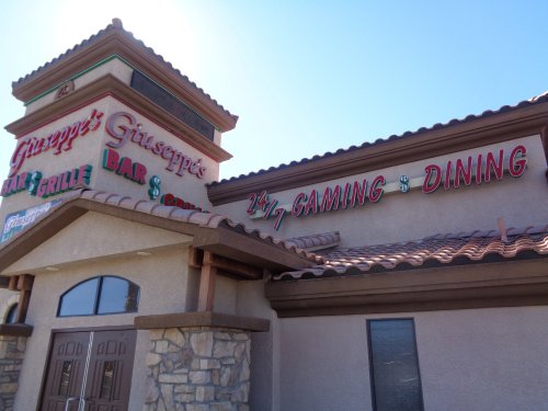 Exterior of Giuseppe's Bar & Grille, featuring a sign for 24/7 gaming and dining, with a tiled roof and stone accents.