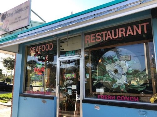 A colorful seafood restaurant with a sign reading "Open" and "Fresh Conch" in the window.