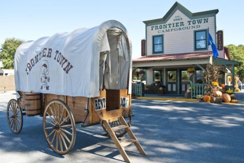 A wooden wagon with a canvas cover labeled "Frontier Town" in front of a campground building with pumpkins.