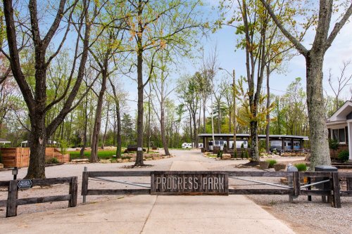 Entrance to Progress Park, featuring a wooden gate, trees, and a pathway leading to a building in the background.