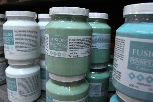Jars of paint in various shades, labeled "Fusion Penney & Co," stacked on a shelf.