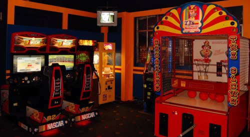 A colorful arcade featuring racing games and a basketball shooting game in a vibrant, playful setting.