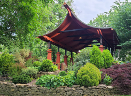 A red-roofed gazebo surrounded by lush greenery and colorful plants in a serene garden setting.