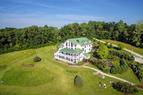 Aerial view of a large house with a green roof, surrounded by lush greenery and landscaped gardens.