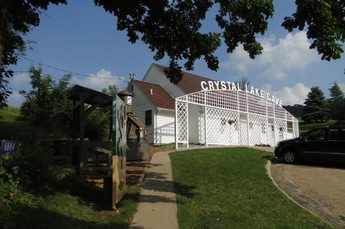 Exterior of Crystal Lake Cave building with a white lattice entrance, surrounded by greenery and a clear blue sky.