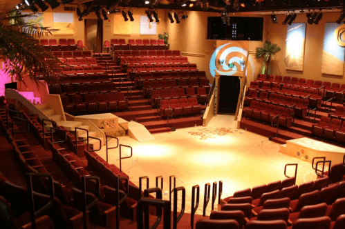 A spacious theater with red seating, a central stage, and colorful decor, ready for a performance.