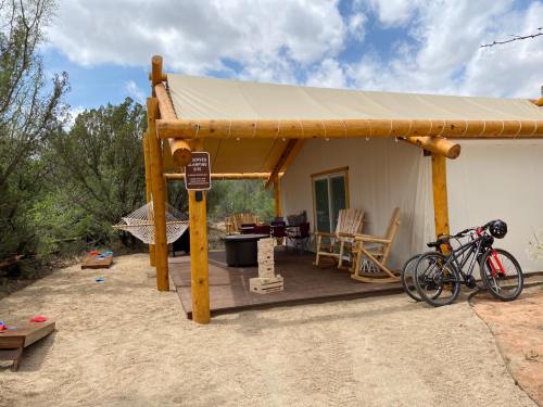A cozy outdoor space with a tented porch, rocking chairs, a fire pit, and bicycles nearby, surrounded by greenery.