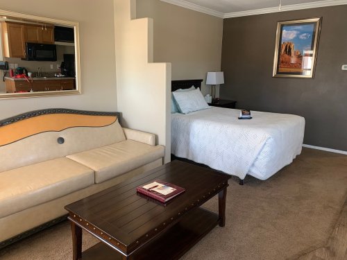 A cozy hotel room featuring a bed, a sofa, a coffee table, and a kitchenette in the background.