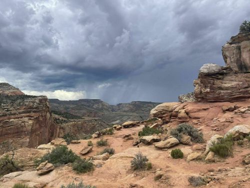 A rocky landscape under a dramatic sky filled with dark clouds, hinting at an approaching storm.