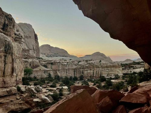 A scenic view of rugged cliffs and canyons at sunset, framed by a rock overhang.