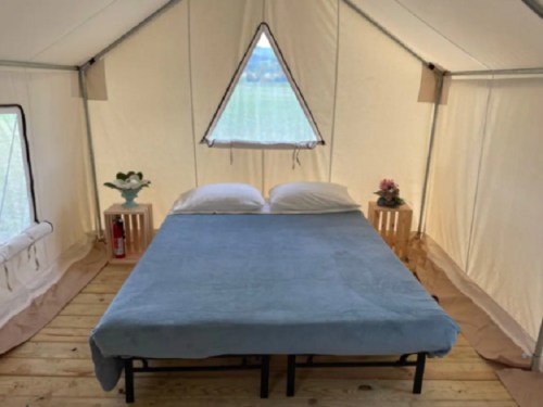 Cozy tent interior with a double bed, two wooden side tables, and a window letting in natural light.